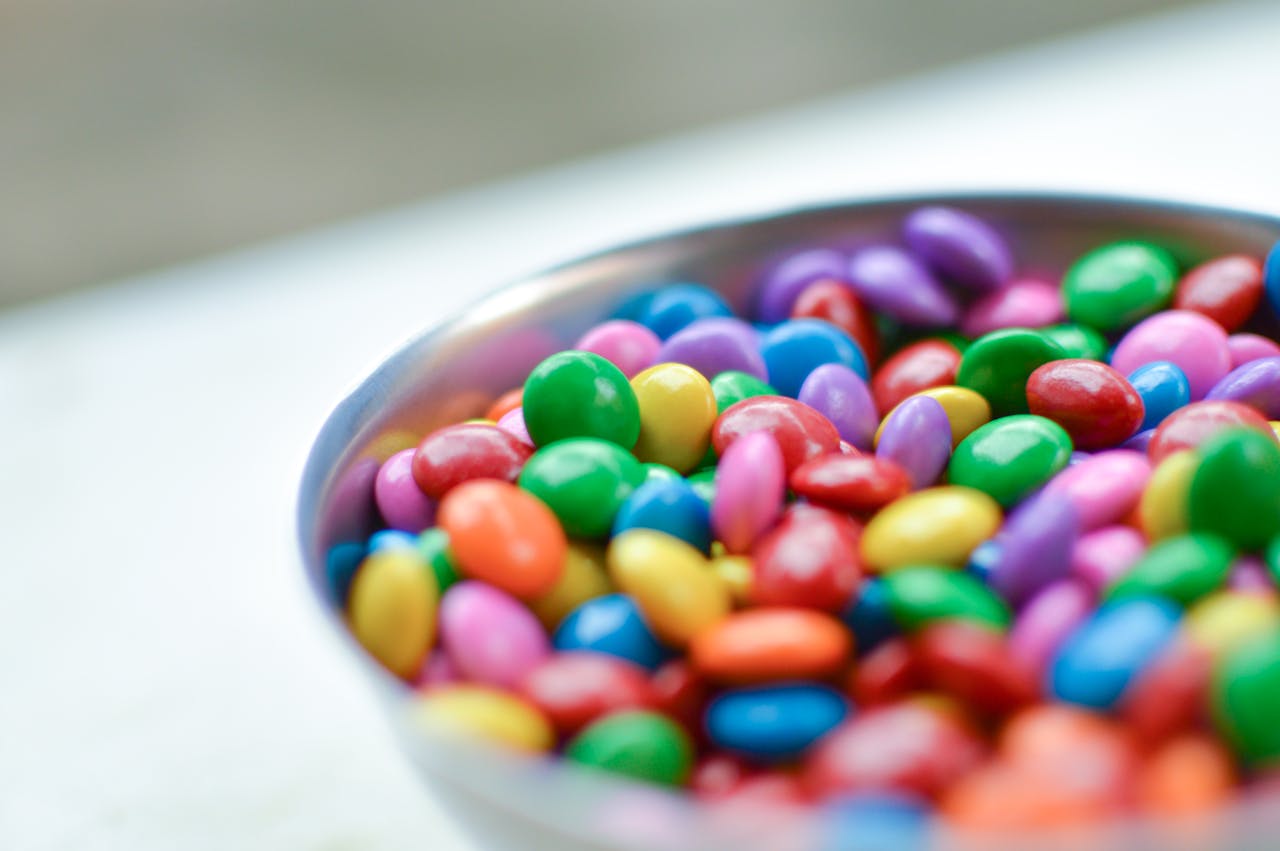 Home Vibrant close-up of assorted candy-coated chocolates in a silver bowl.